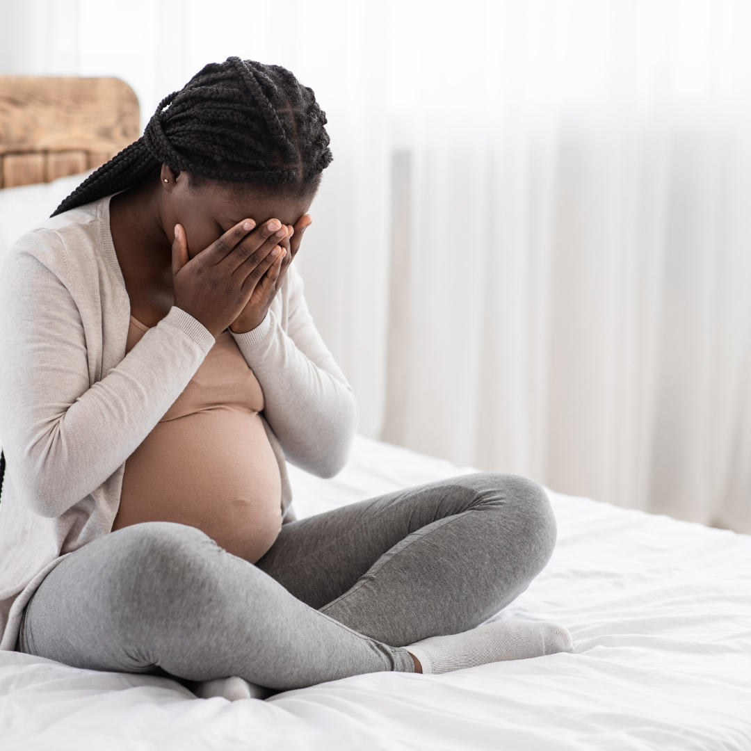 Pregnant woman seated with her face in her hands