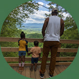 Family of three standing on a wooden deck overlooking a scenic landscape.