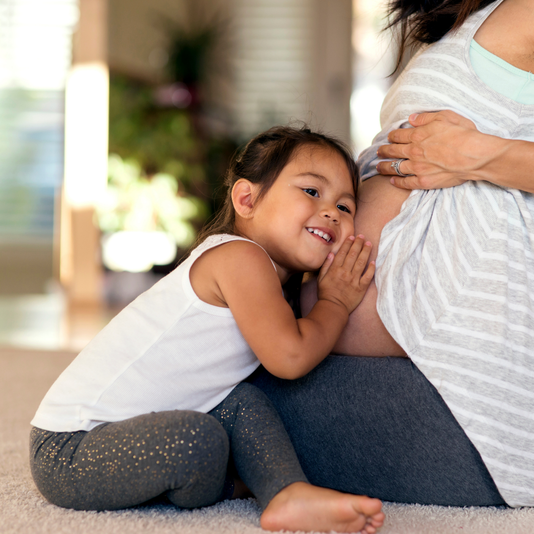 Young child listening at her pregnant mother’s belly