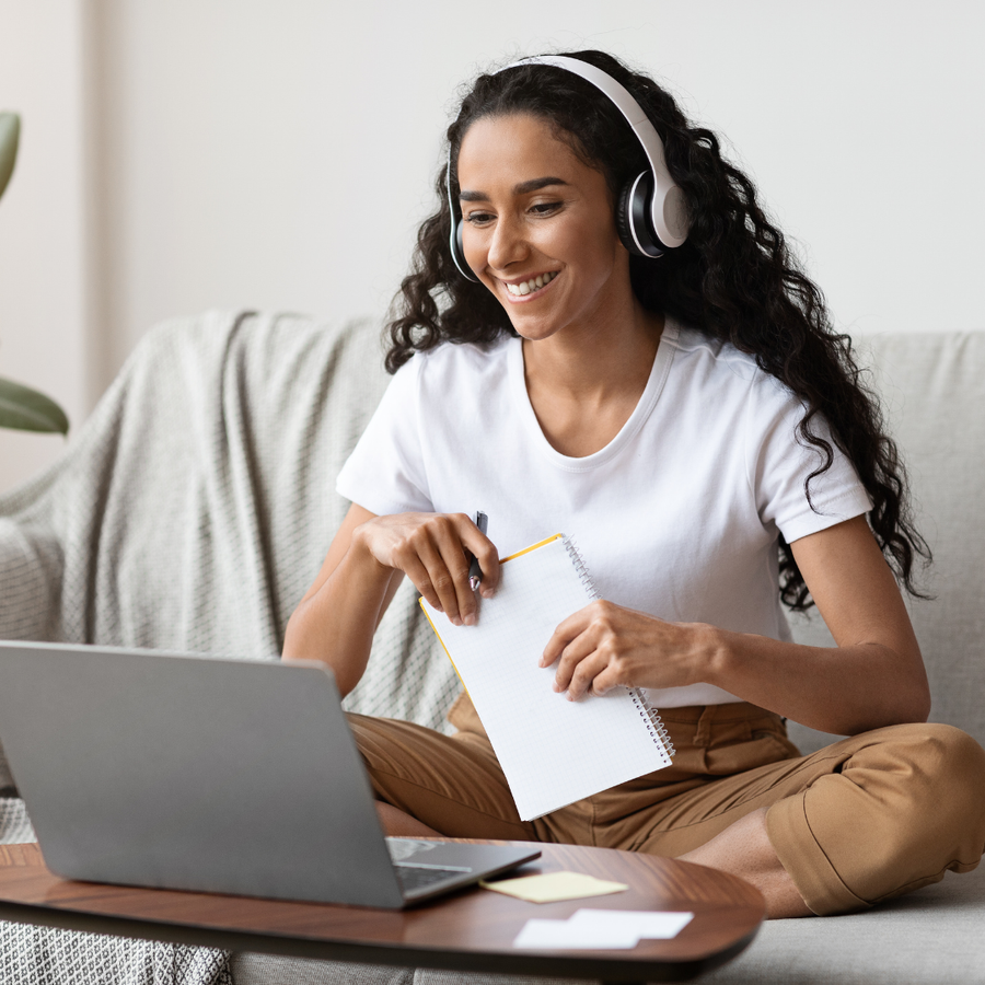 Woman using a laptop while taking notes at home